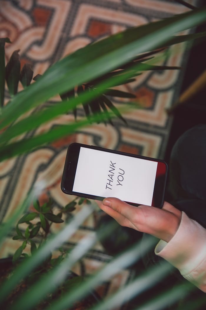 Hand holding smartphone with 'Thank You' message surrounded by lush indoor plants.